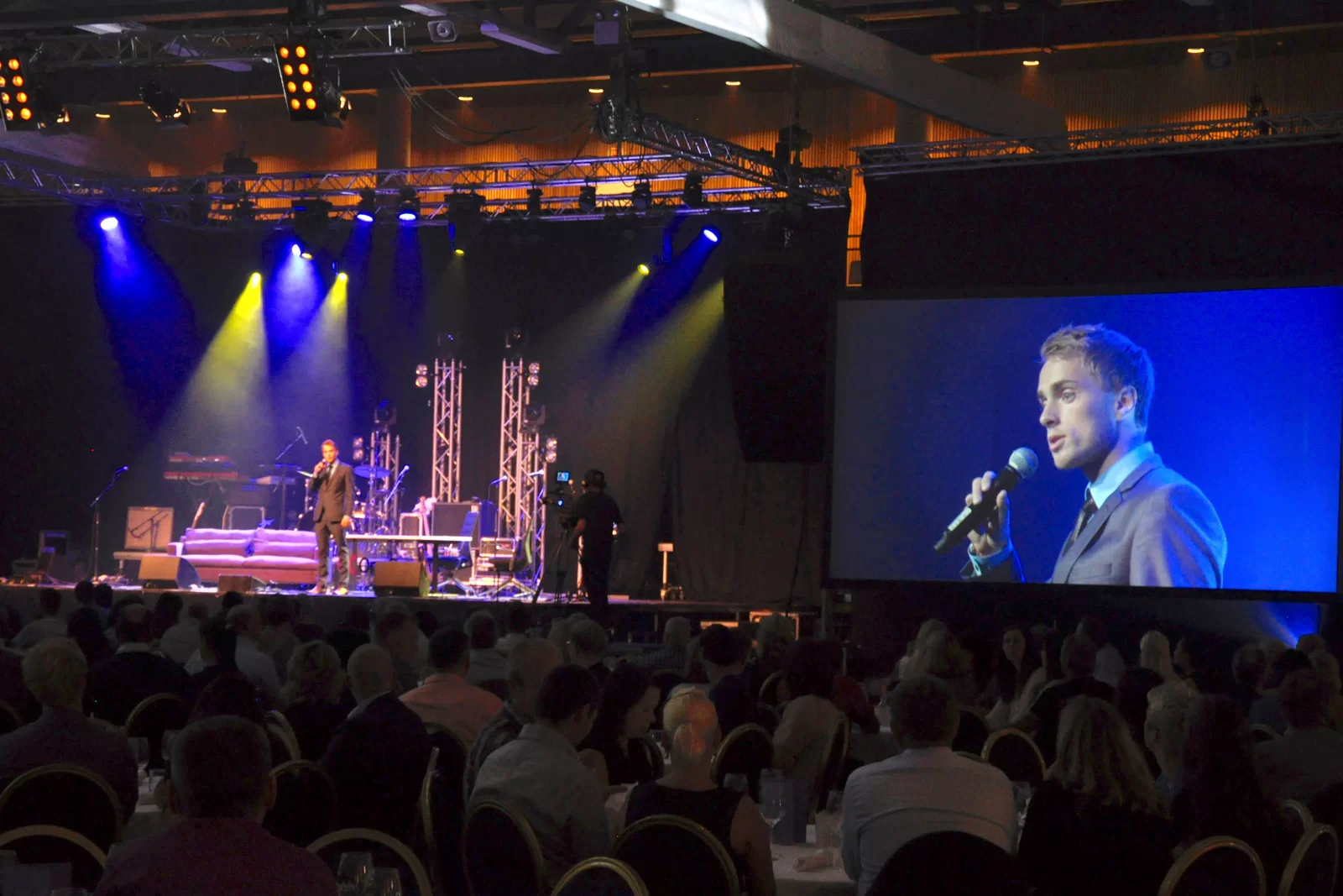 Hans Grane on stage with camera and screen at a large corporate event
